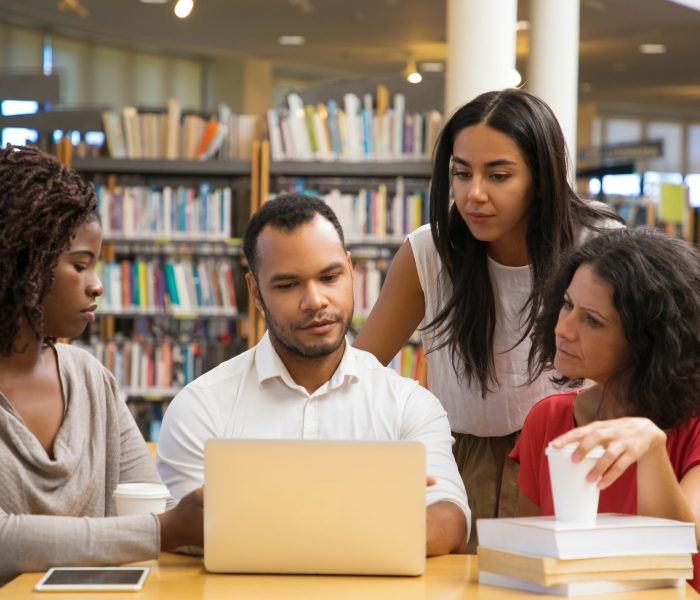 Concentrated young people reading information from laptop. Cheerful students working with laptop at library. Education concept